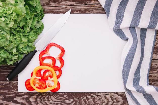 Lechuga y paprika verdes frescos en el Libro Blanco con la servilleta de la raya en la tabla de madera