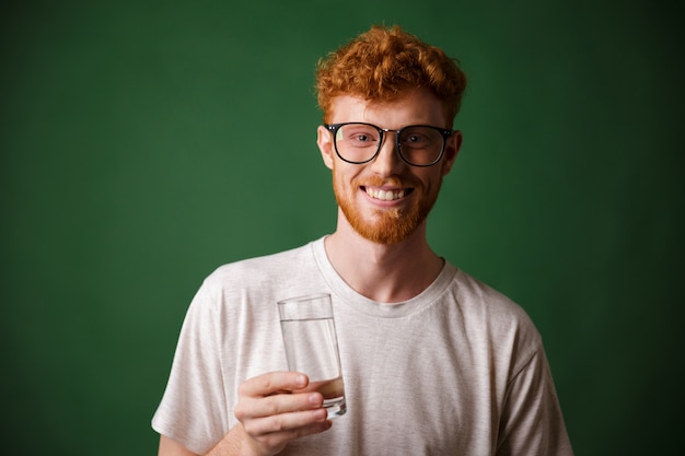 Lectura alegre hombre barbudo con gafas, sosteniendo un vaso de agua,