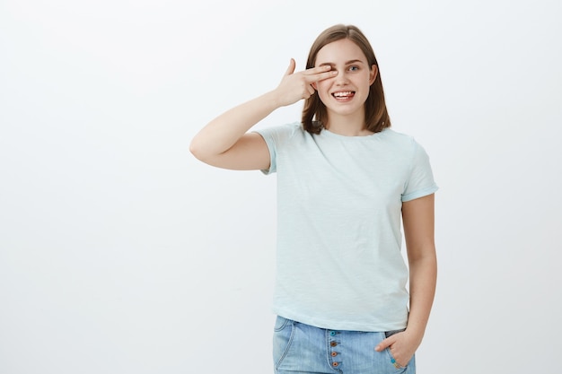 Leer palabras con un ojo en la tienda de óptica, elegir gafas nuevas. Retrato de mujer encantadora de aspecto agradable alegre con cabello castaño corto sosteniendo los dedos a la vista apuntando hacia la derecha y sonriendo con alegría