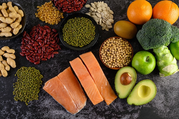 Legumbres, brócoli, fruta y salmón colocados en un piso de cemento negro.