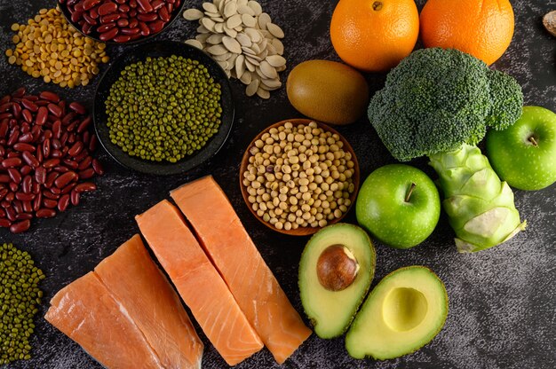 Legumbres, brócoli, fruta y salmón colocados en un piso de cemento negro.