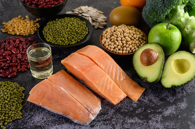 Legumbres, brócoli, fruta y salmón colocados en un piso de cemento negro.