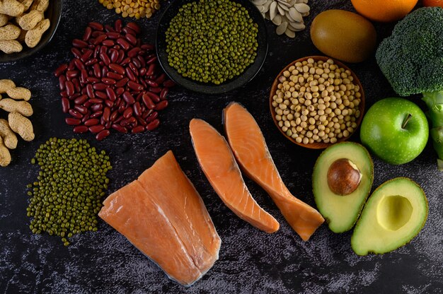 Legumbres, brócoli, fruta y salmón colocados en un piso de cemento negro.