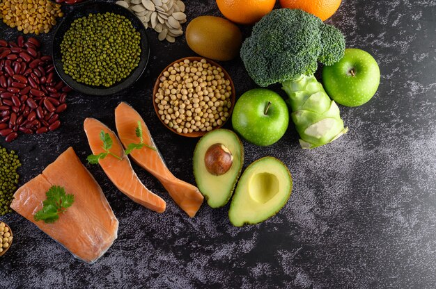 Legumbres, brócoli, fruta y salmón colocados en un piso de cemento negro.