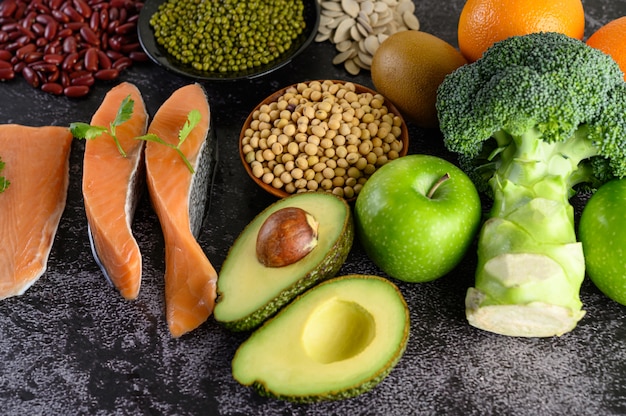 Legumbres, brócoli, fruta y salmón colocados en un piso de cemento negro.