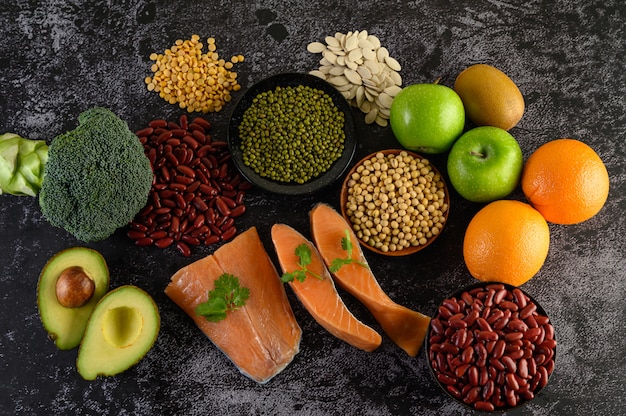 Legumbres, brócoli, fruta y salmón colocados en un piso de cemento negro.