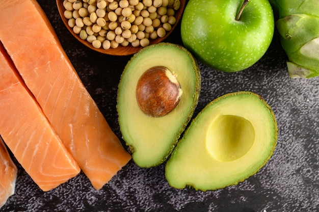 Legumbres, fruta y salmón colocados en un piso de cemento negro.