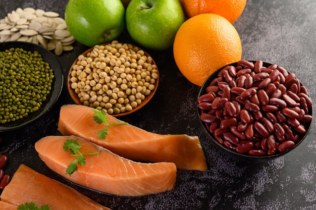 Legumbres, fruta y salmón colocados en un piso de cemento negro.