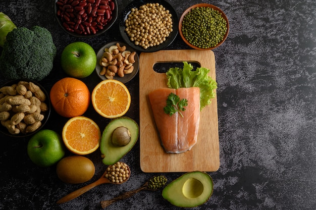 Legumbres, frutas y piezas de pescado de salmón en una tabla de cortar de madera.