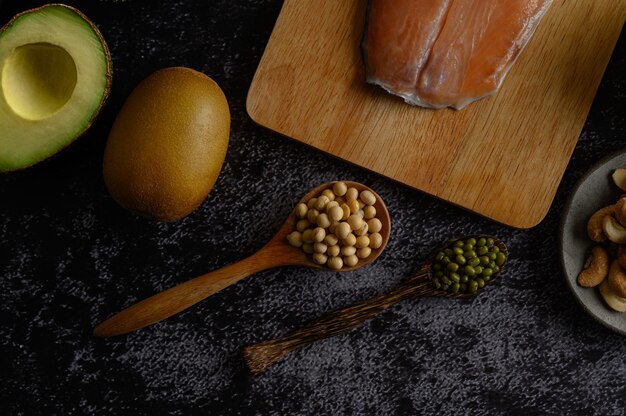 Legumbres, trozos de salmón y kiwi sobre una superficie de piso de cemento negro.