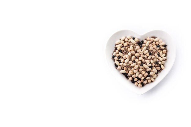 Legumbres variadas crudas en placa con forma de corazón aisladas en fondo blanco