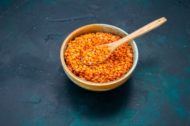 Lenteja naranja cruda de media vista superior dentro de una olla redonda con cuchara de madera en el escritorio azul oscuro.