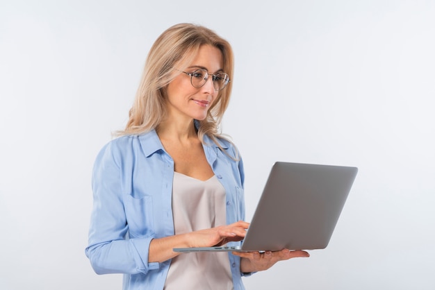 Lentes que desgastan de la mujer joven que usan la computadora portátil contra el fondo blanco