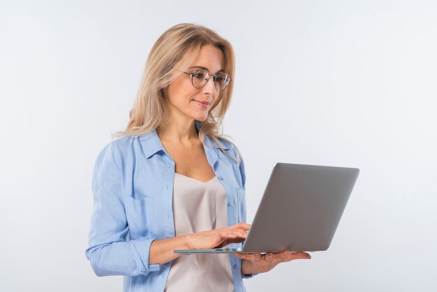 Lentes que desgastan de la mujer joven que usan la computadora portátil contra el fondo blanco