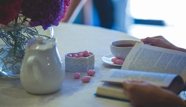 Leyendo un libro con una taza de té y dulces rosados a un lado