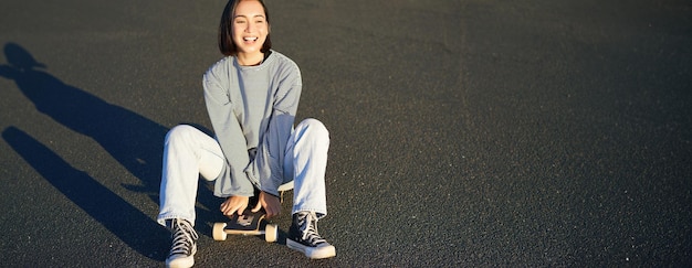 Foto gratuita libertad y felicidad una chica asiática sonriente y linda se sienta en patineta en un soleado día de primavera riendo feliz