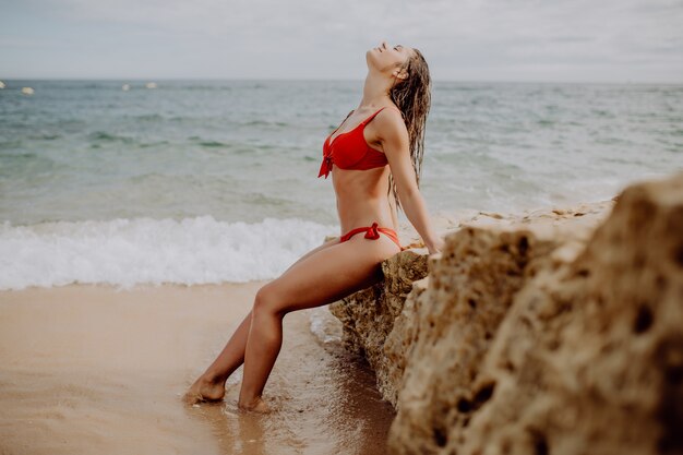 Libertad Mujer joven en bikini rojo sentada en el acantilado cerca de Sea Alone. Vocación de verano
