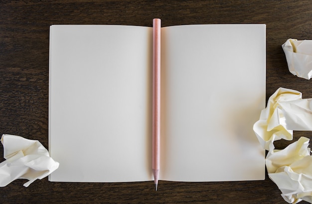 Libro abierto en blanco sobre una mesa de madera con un lápiz enmedio