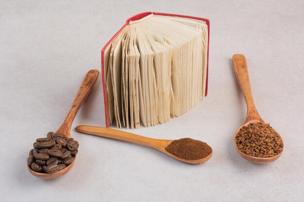 Un libro abierto con cucharas de madera llenas de granos de café y cacao en polvo. Foto de alta calidad