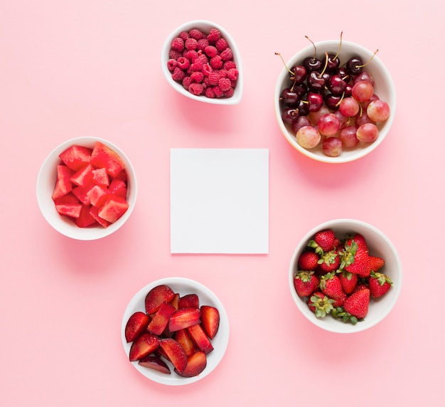 Libro blanco en blanco con tazones de frutas de color rojo sobre fondo rosa