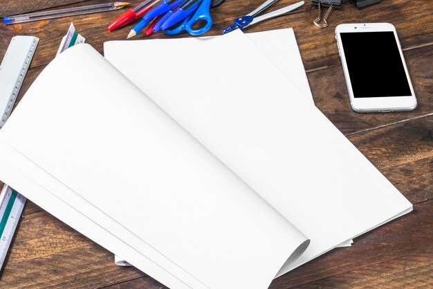 Libro blanco con papelería y teléfono inteligente en la mesa de madera