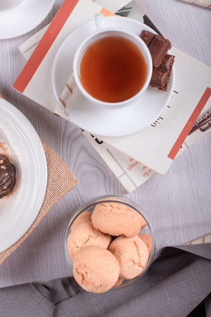 Libro, bocadillos dulces y una taza de té sobre la mesa.