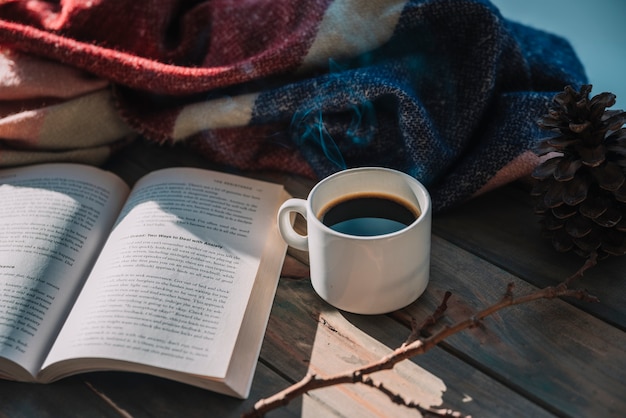 Libro cerca de taza y cuadros de lana en mesa