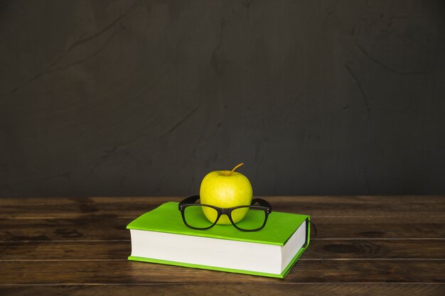 Libro colorido con gafas y manzana en el escritorio