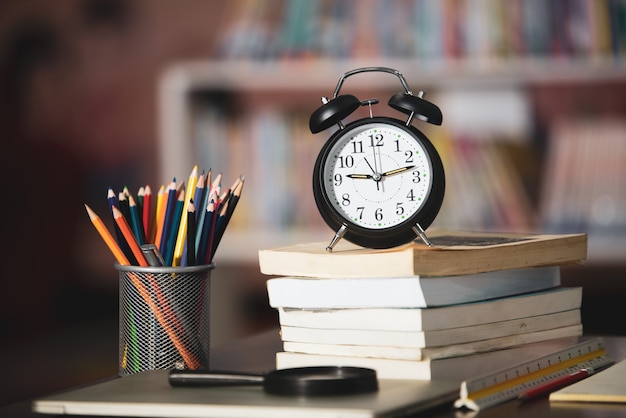 Libro, computadora portátil, lápiz, reloj en la mesa de madera en la biblioteca, concepto de aprendizaje educativo