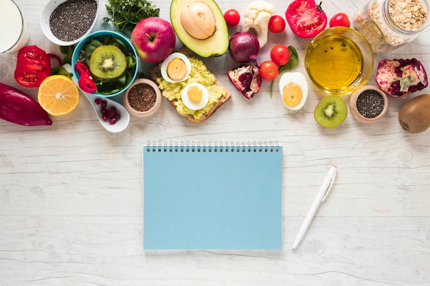 Libro de espiral bolígrafo; frutas frescas; pan tostado; Verduras e ingredientes sobre fondo blanco con textura