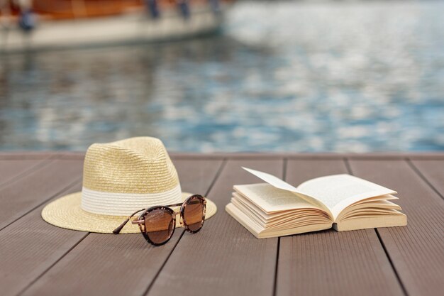 Libro de gafas de sol y un sombrero de pie en la orilla de un puerto