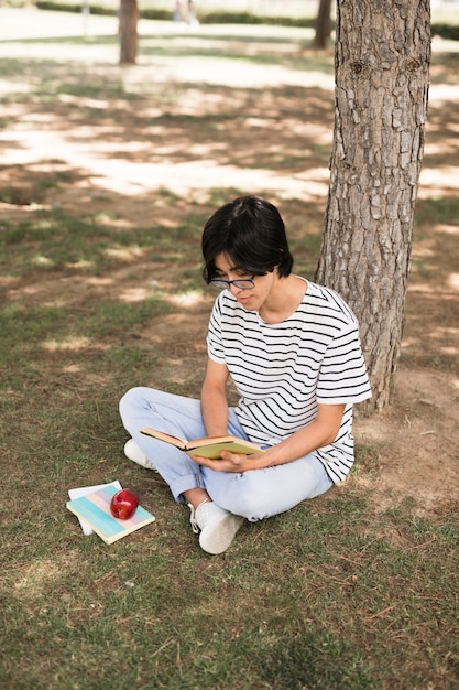 Libro de lectura adolescente asiática del estudiante debajo del árbol