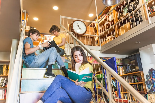 Libro de lectura adolescente en pasos cerca de compañeros de clase