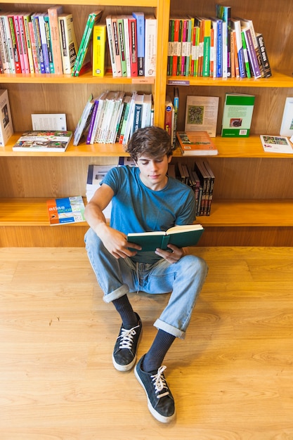 Foto gratuita libro de lectura adolescente relajado en el piso de la biblioteca