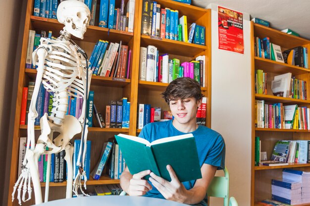 Libro de lectura adolescente sonriente en la mesa de la biblioteca