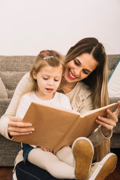 Libro de lectura alegre de la madre a la hija cerca del sofá