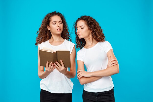 Libro de lectura de dos gemelos de mujer sobre azul.