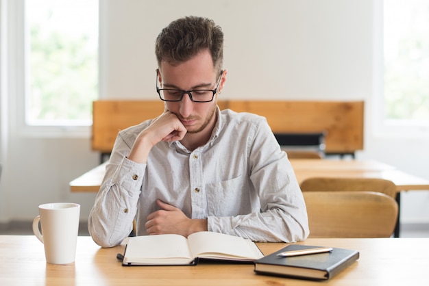 Libro de lectura enfocado del estudiante masculino en el escritorio en sala de clase