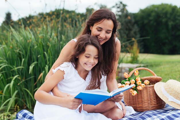 Libro de lectura feliz de la madre y de la hija en la comida campestre