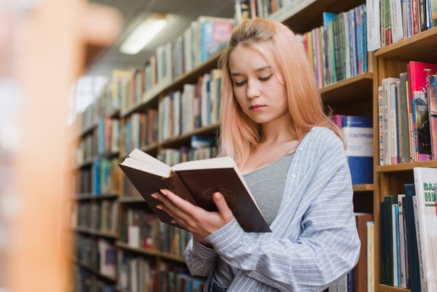 Libro de lectura femenina adolescente cerca de estanterías