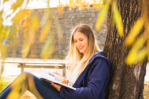 Libro de lectura femenino atractivo debajo de la corona del árbol de la caída