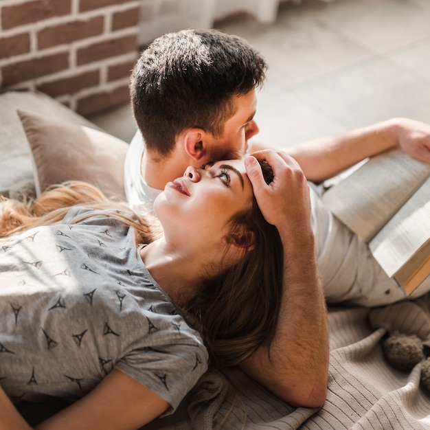 Libro de lectura del hombre cerca de la mujer que miente en su cabeza en casa