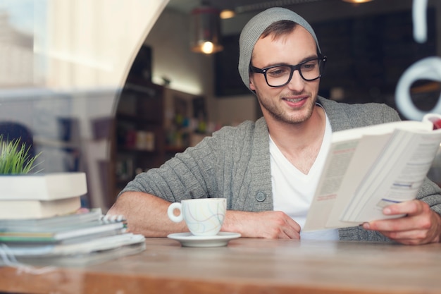 Libro de lectura de hombre hipster sonriente en el café