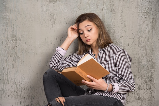 Libro de lectura de joven estudiante cuidadosamente sobre muro de piedra