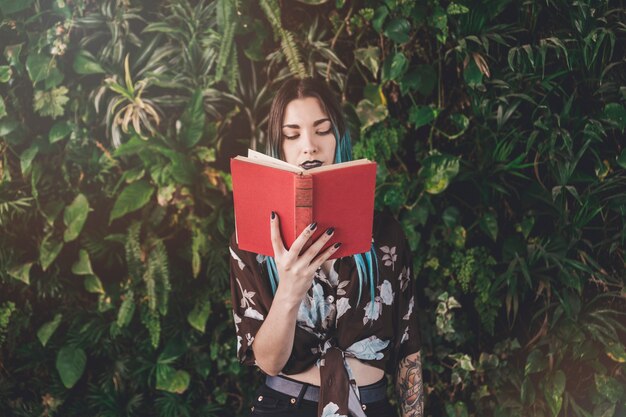 Libro de lectura moderno de la mujer joven que se coloca delante de las plantas crecientes