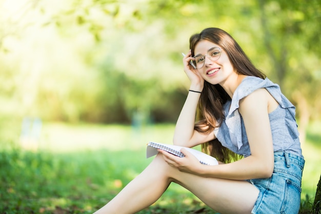 Libro de lectura de mujer joven bajo el árbol durante un picnic en la luz del sol de la tarde