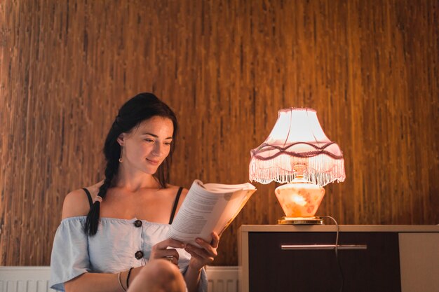 Libro de lectura de la mujer joven cerca de la lámpara de luz iluminada