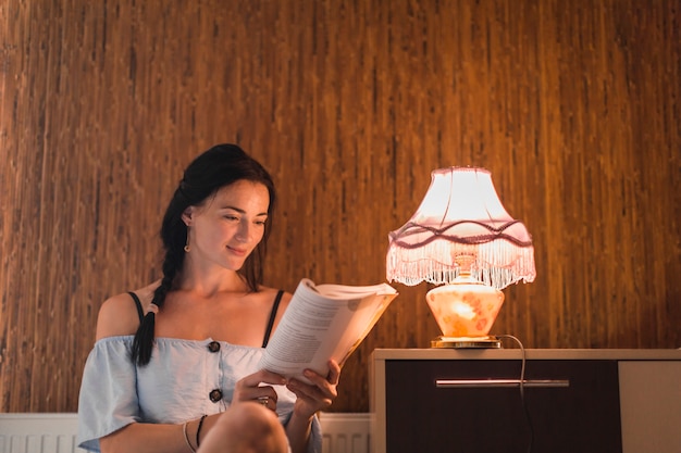 Libro de lectura de la mujer joven cerca de la lámpara de luz iluminada