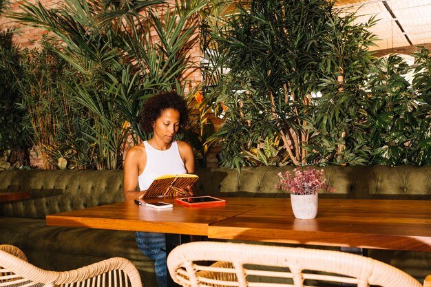 Libro de lectura de la mujer joven que se sienta cerca de la tabla en el restaurante