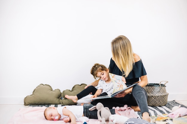 Libro de lectura de mujer y niña cerca de bebé